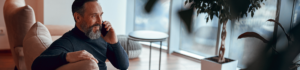 Bearded man talking on a phone while sitting on a sofa in a modern office lounge.