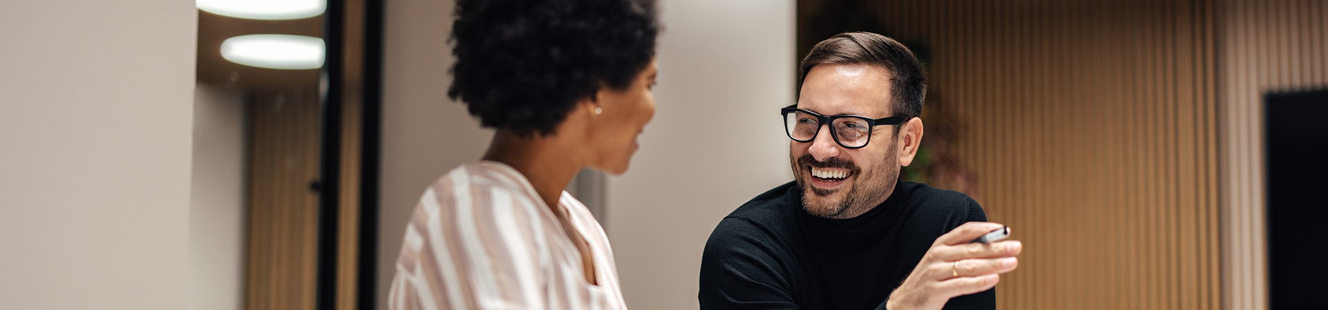 Two coworkers smiling and talking during a meeting in a office.