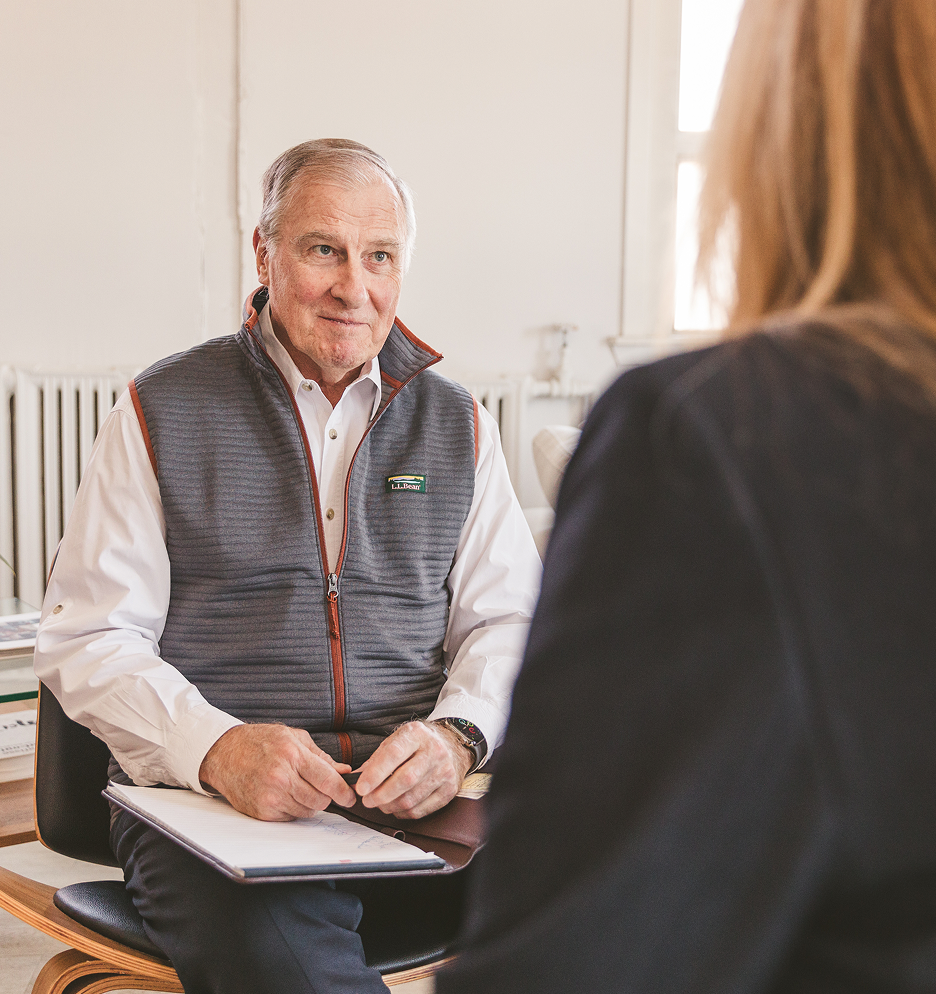 Older man holding a notebook while speaking with a woman