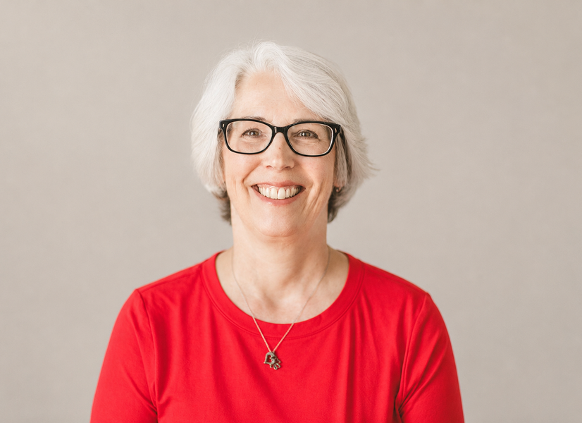 Professional headshot of a woman smiling with black glasses and a red shirt.