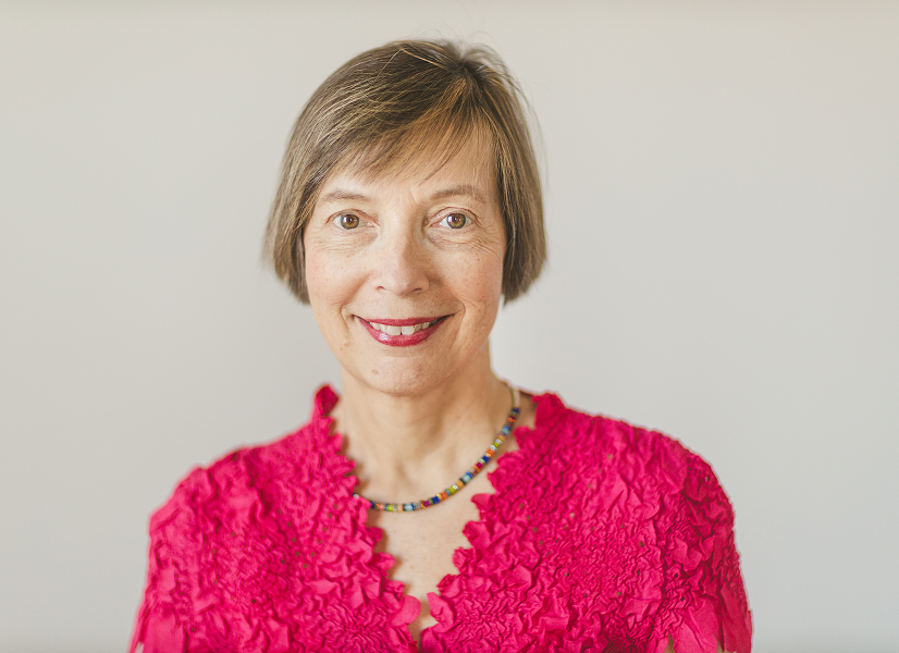 Professional headshot of an woman smiling in a pink blouse and colourful necklace.