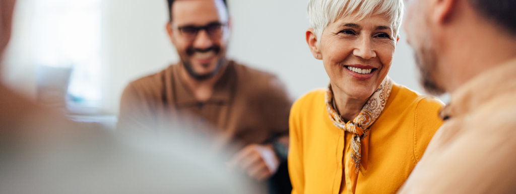 Older woman smiling while talking with colleagues during a group meeting.