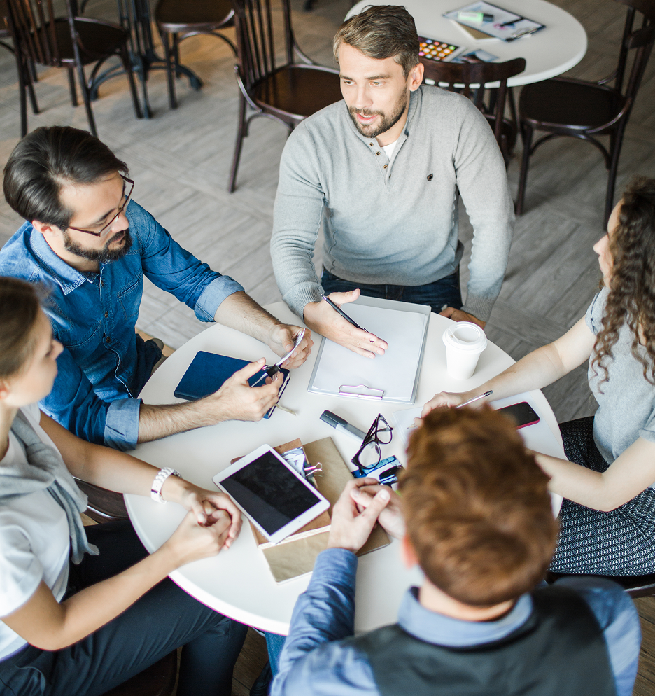 Five coworkers discussing ideas around a table with notebooks, a tablet and coffee.