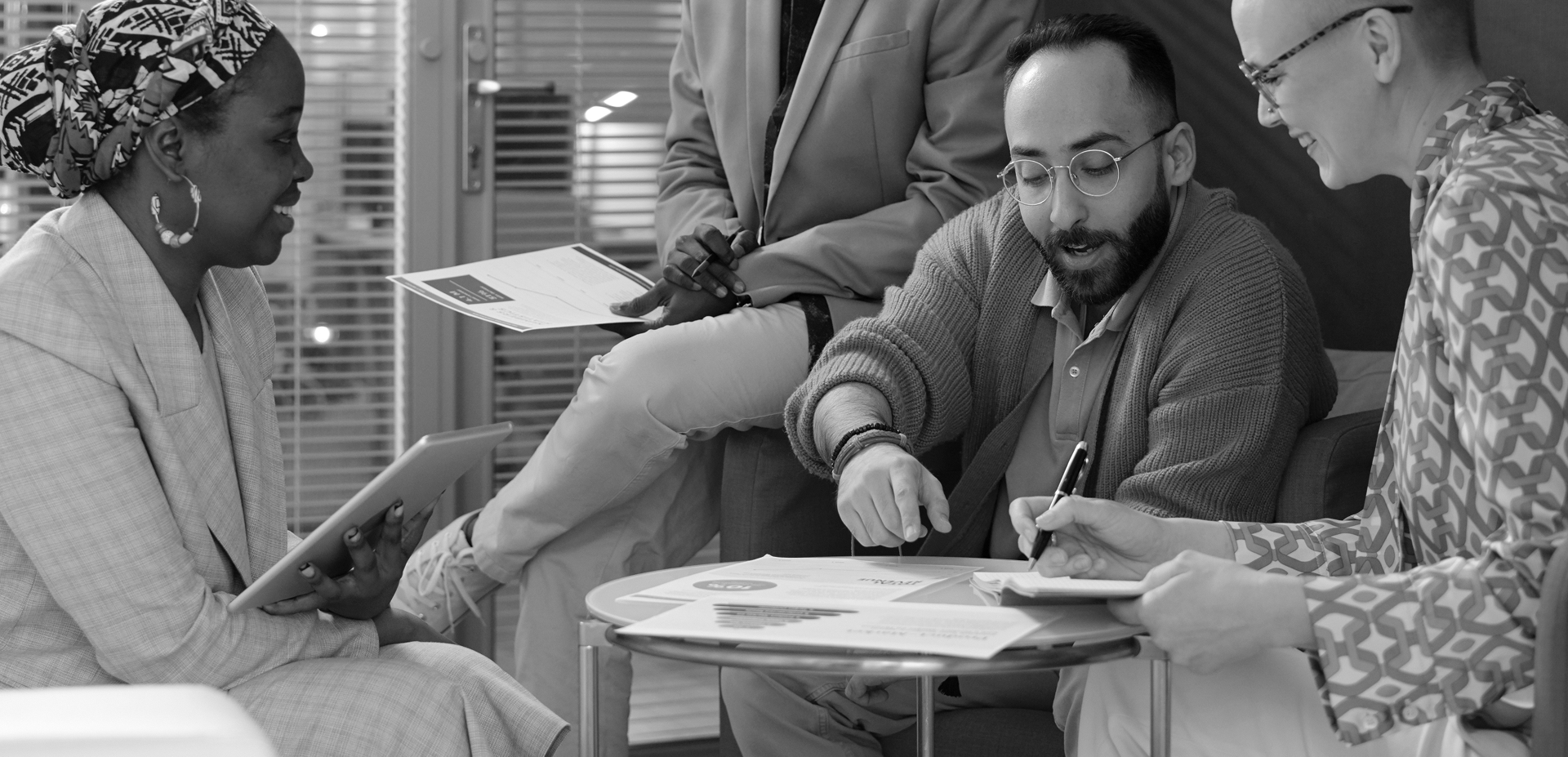 Four coworkers reviewing paperwork and taking notes during a group chat.