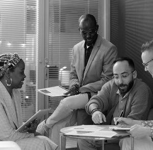 Four coworkers reviewing paperwork and taking notes during a group chat.