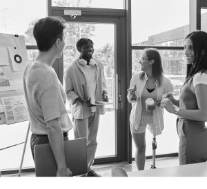 Four coworkers talking beside a presentation board with charts in a office.