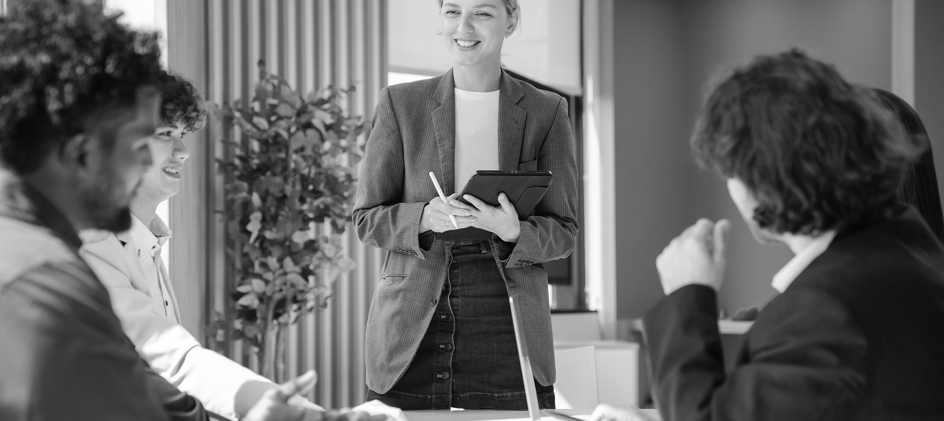 Woman holding a tablet while leading a discussion with colleagues in an office.