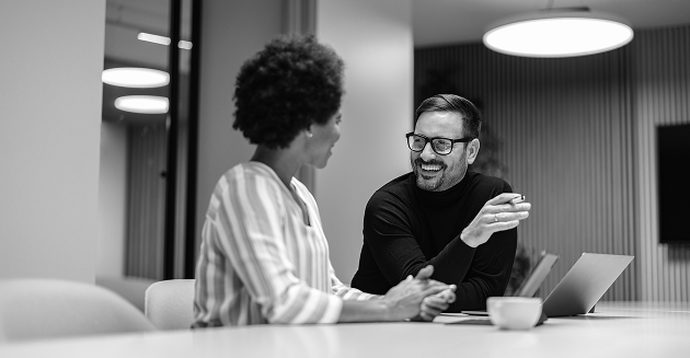 Two coworkers smiling and talking during a meeting in a office.